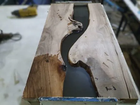 artisan pouring epoxy resin into walnut mold during epoxy coffee table production