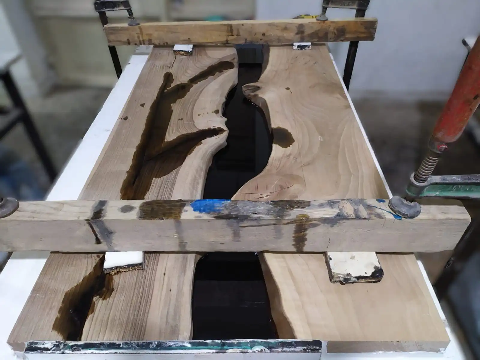 artisan pouring epoxy resin into walnut mold during coffee table manufacturing process