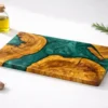 An overhead studio shot of a bespoke Olive Wood Epoxy Cutting Board showcasing wild olive grain and custom liquid resin channels against a crisp white background.