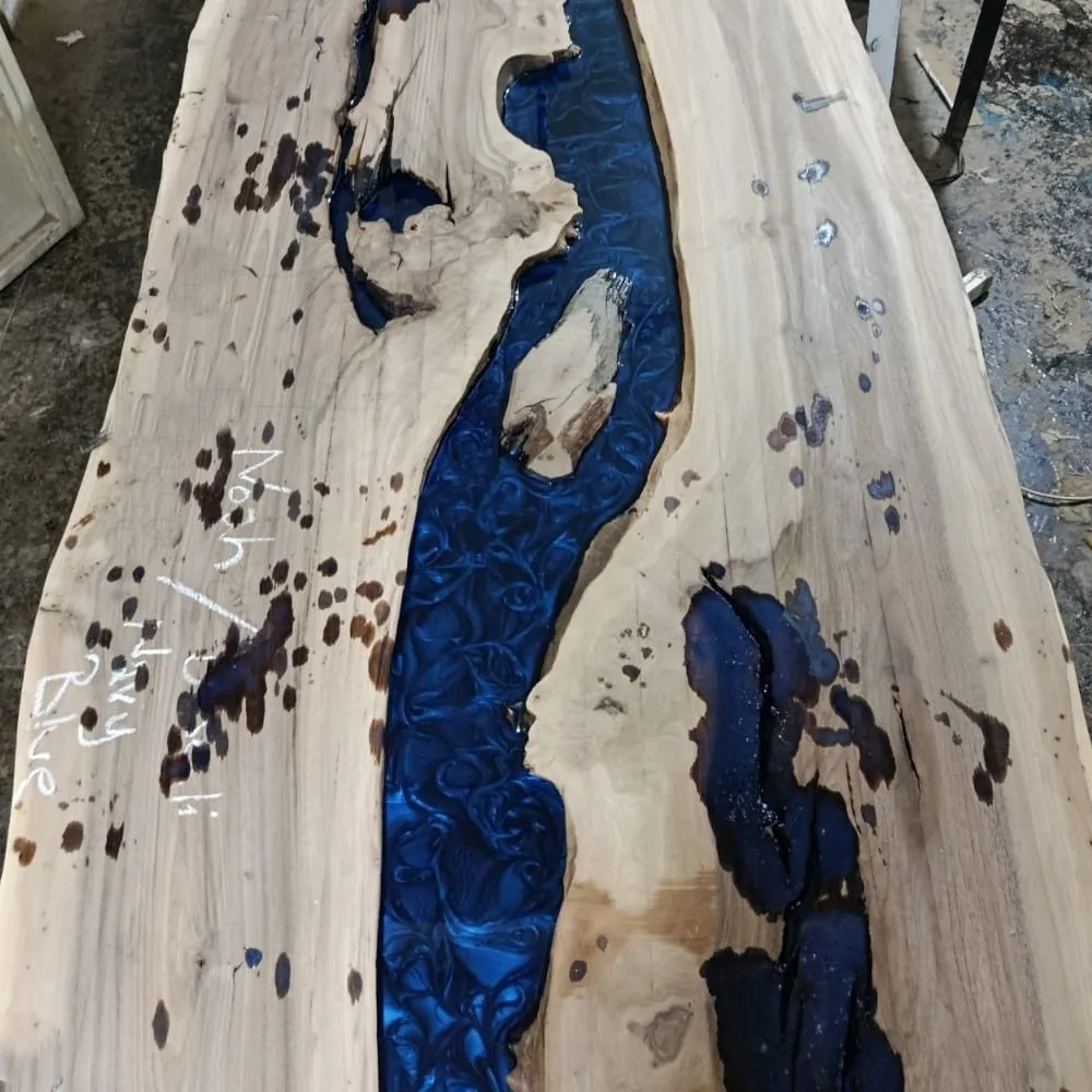 Liquid navy blue epoxy resin being poured into river channel between live edge walnut slabs in climate-controlled studio.